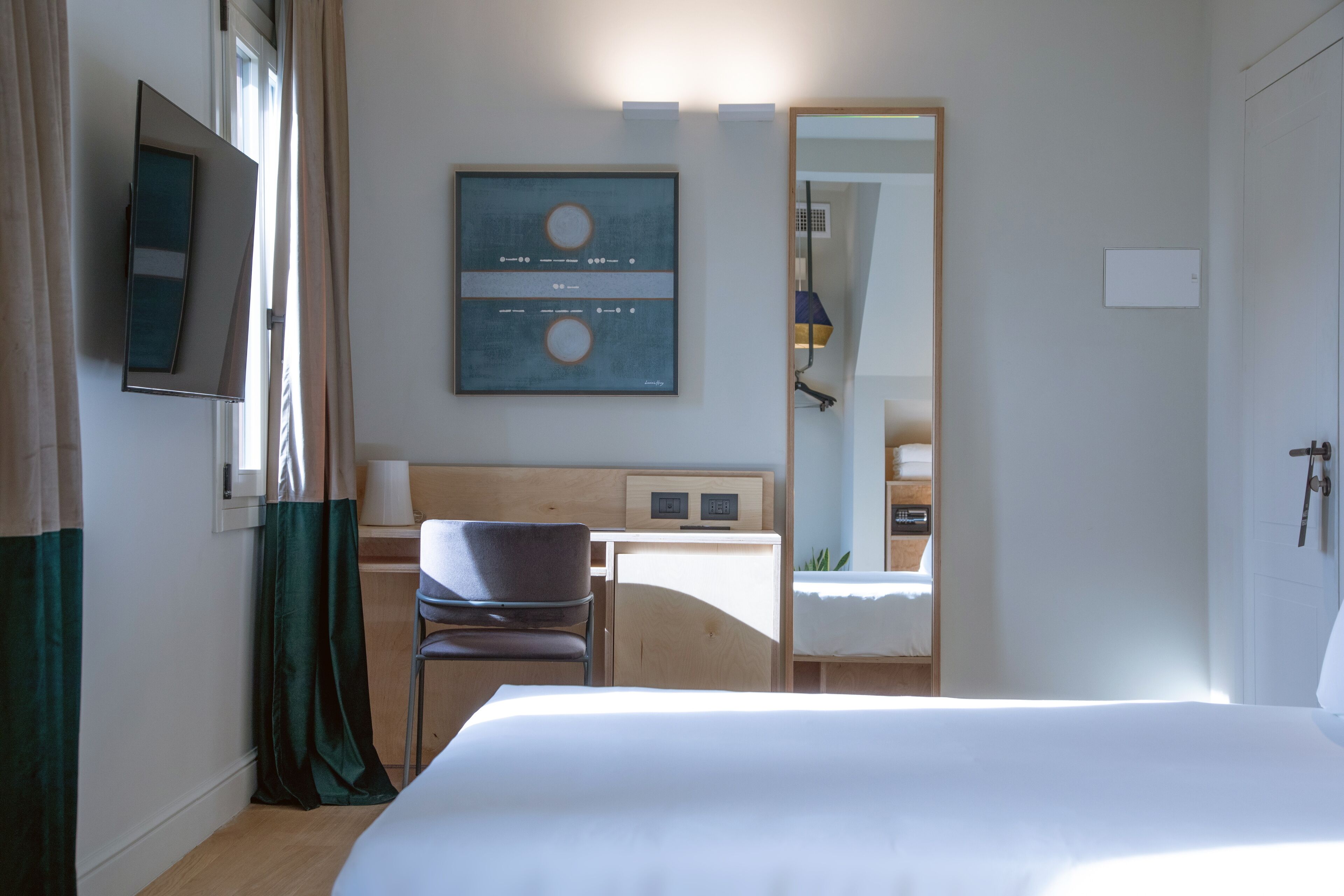 Habitación de hotel con cama, escritorio, silla, televisor y una obra de arte enmarcada en la pared.