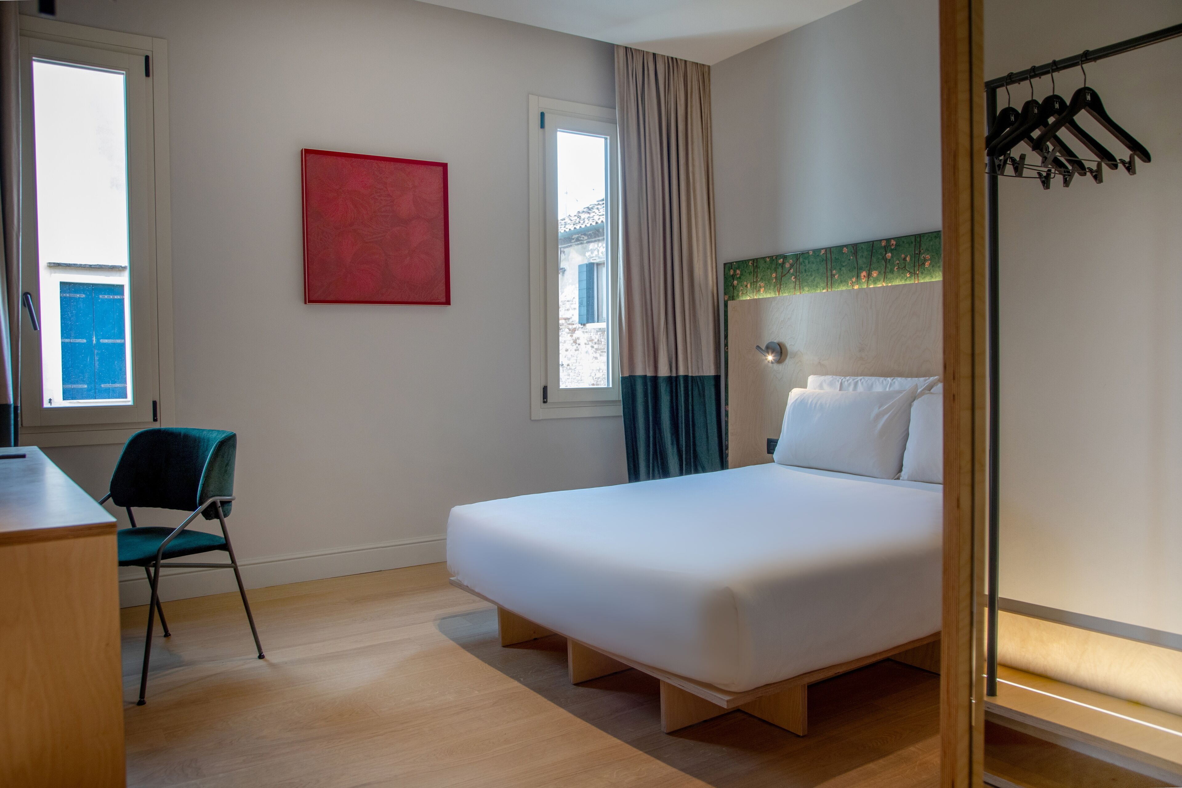 Una habitación de hotel con una cama, un escritorio, una silla y un ventanal con cortinas.