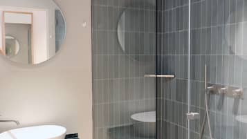 Un bagno moderno con cabina doccia in vetro, uno specchio rotondo, un lavandino bianco e un piano d'appoggio in marmo.