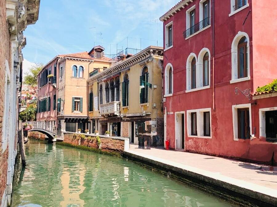 Un canal étroit, bordé de bâtiments historiques aux fenêtres en arc et aux balcons, dont le reflet se mire dans l’eau.