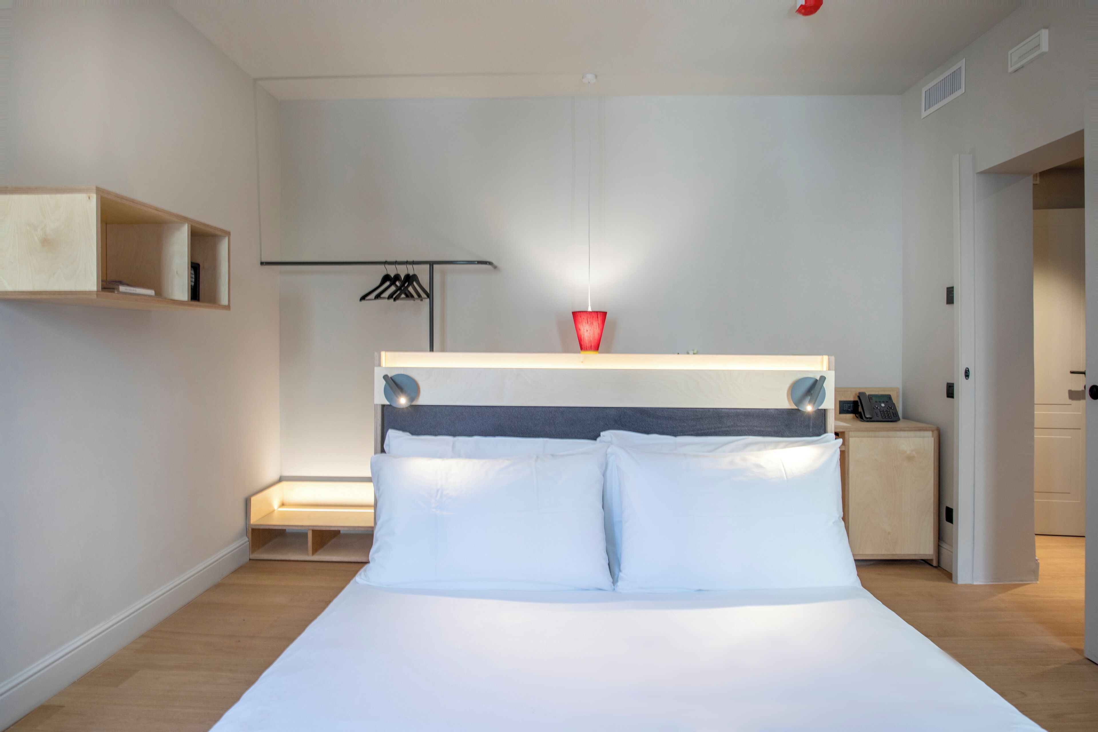 A modern hotel room with a bed, bedside table, and a small cabinet.