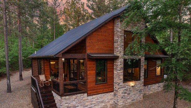 A cabin with a stone exterior, wooden siding, and a covered porch with seating.