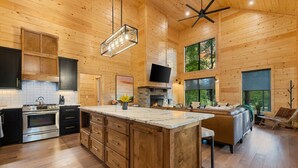 A spacious kitchen with wooden cabinetry, a large island, and a stone fireplace.