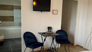 Habitació moderna amb un llit, una televisió, dues cadires blaves, una taula petita i una làmpada de sostre singular.