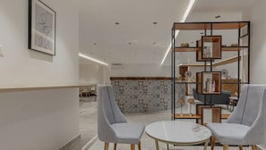 A modern interior with two grey armchairs, a round white table, and a wooden bookshelf with decorative items. - Akoya Business Hotel - Smart Stays, Whitefield (Bengaluru)