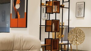A modern living room with a white leather armchair, a wooden bookshelf, and a round table with a decorative item. - Akoya Business Hotel - Smart Stays, Whitefield (Bengaluru)