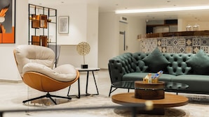 A modern living room with a leather armchair, a tufted sofa, and a coffee table with a decorative centerpiece. - Akoya Business Hotel - Smart Stays, Whitefield (Bengaluru)