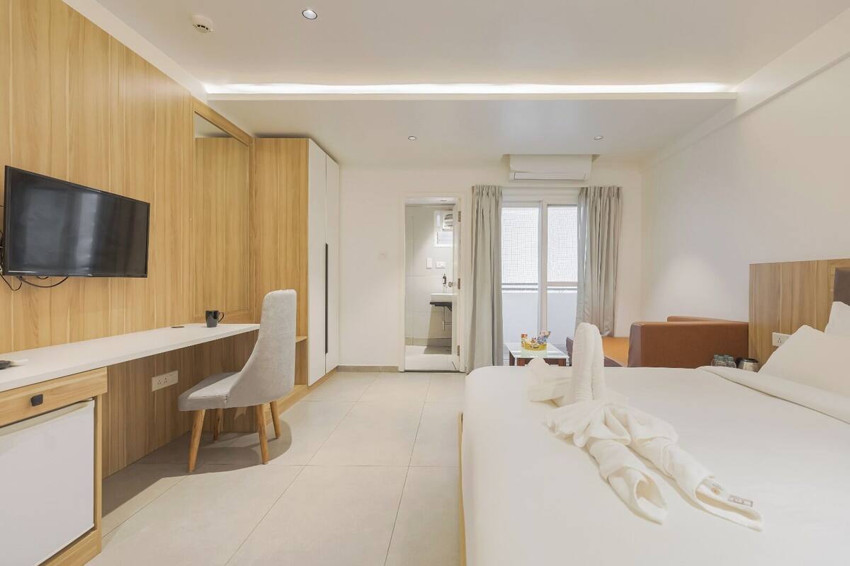 A hotel room with a bed, a desk, a chair, a television, and a bathroom visible through an open door.