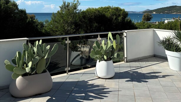Eine Terrasse mit Kakteen in Töpfen und Blick aufs Meer.