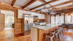 Une cuisine spacieuse avec des poutres en bois, des appareils électroménagers en acier inoxydable et un îlot central doté de tabourets de bar.