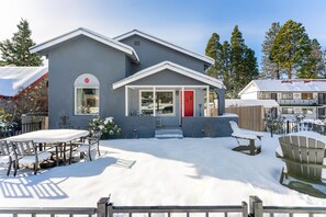 A modern house with a red door, a covered patio with outdoor furniture, and a snow-covered yard.