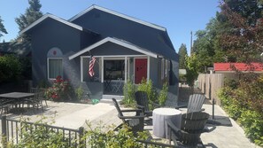 A two-story house with a red door and an American flag. There is a patio with outdoor furniture and a garden.