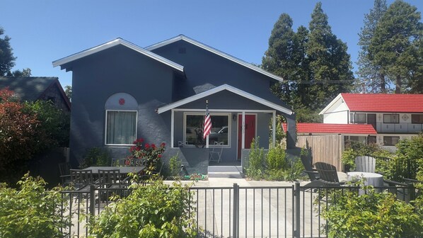 A two-story house with a dark exterior, a red door, and a front porch with a flag.