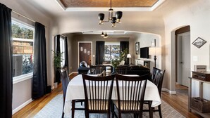 Een eetruimte met een ronde tafel, stoelen en een kroonluchter. Er is uitzicht naar buiten door een raam.