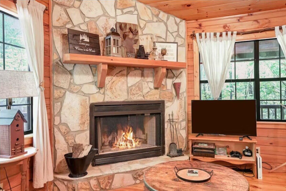 Interior acogedor de una cabaña con chimenea de piedra, un televisor y una mesa de madera.