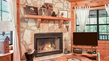Interior acogedor de una cabaña con chimenea de piedra, un televisor y una mesa de madera.