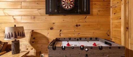 A wooden room with a dartboard, a foosball table, and a lamp.