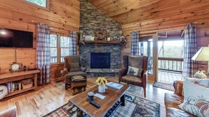 A cozy cabin interior with a stone fireplace, wooden walls, and plaid curtains.