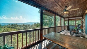 Una terraza de madera con una mesa y sillas, con vistas a un paisaje boscoso y montañas a lo lejos.