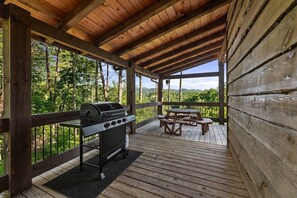 A covered outdoor area with a grill and picnic table, surrounded by a wooden deck and overlooking a forested landscape. - Pony Ghost Trail - A cabin and view to remember (Blue Ridge)