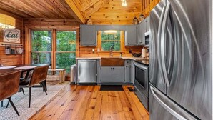 Una cocina tipo cabaña con paredes de madera, un refrigerador de acero inoxidable y un comedor con mesa y sillas.