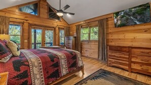 Un dormitorio de cabaña de madera con una cama, un ventilador de techo y un cuadro de una cascada.