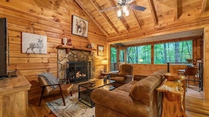 A cozy cabin interior with a stone fireplace, leather furniture, and large windows overlooking a forest. - Wine Knot in Blue Ridge (Blue Ridge)