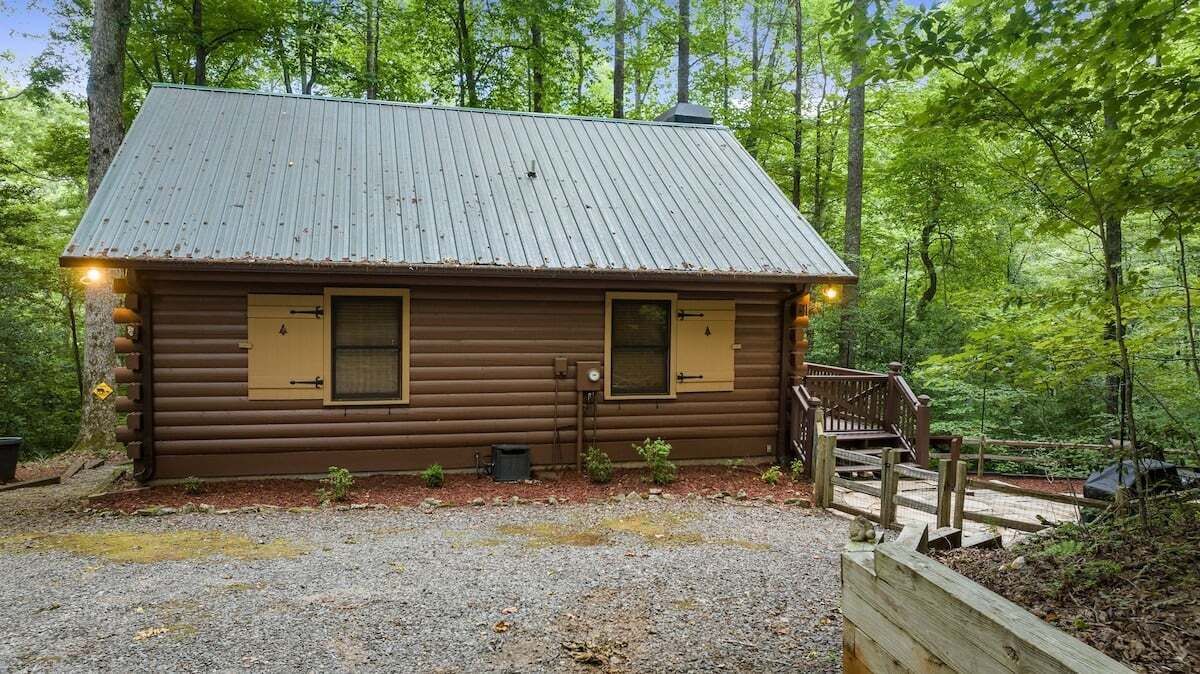 A log cabin with a metal roof, two windows, and a wooden porch.
