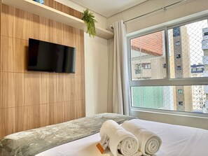 Quarto com cama de casal, TV na parede e movel de madeira clara.