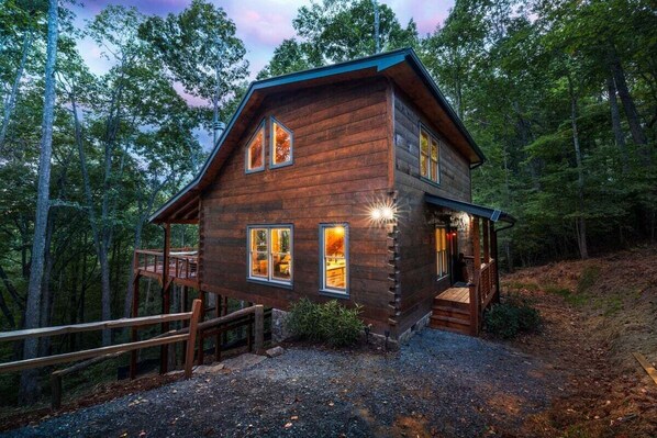 A wooden cabin with a deck, surrounded by trees.