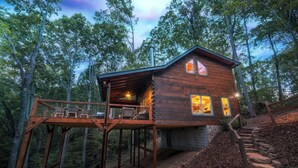 Una baita di legno con veranda e struttura in vetro, immersa tra gli alberi.