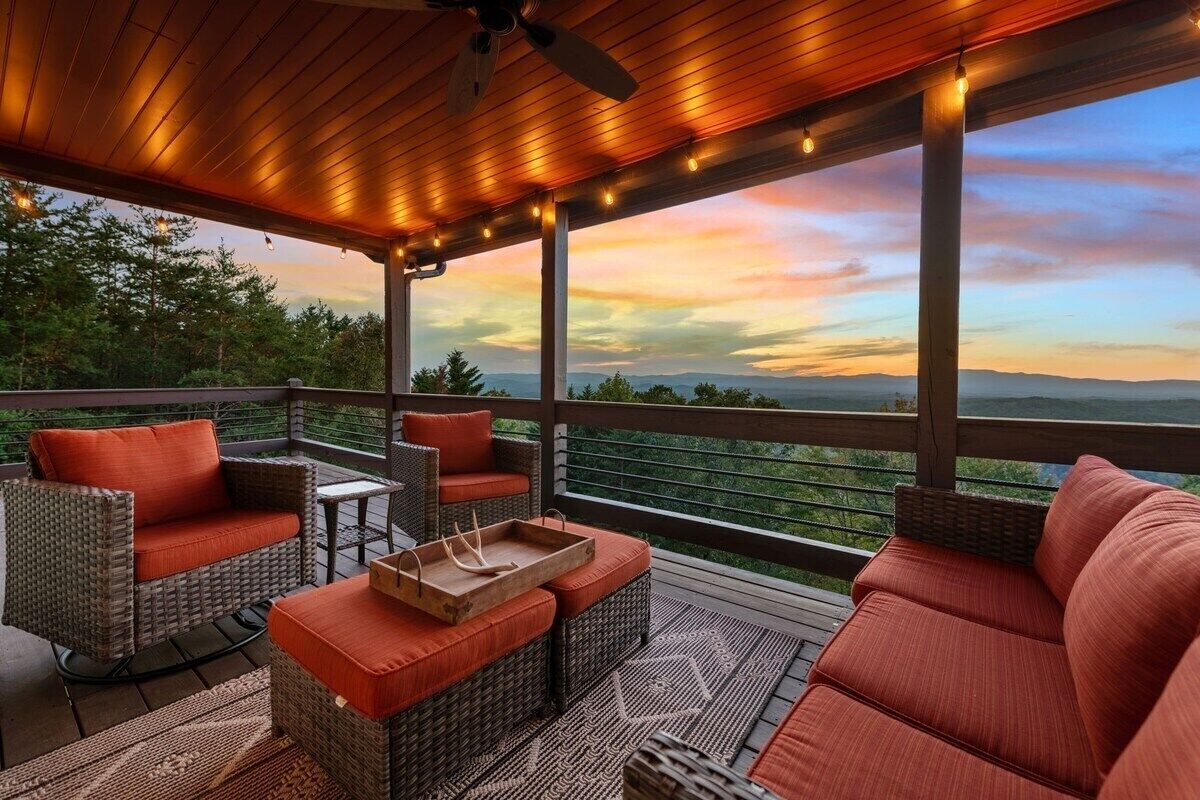 A covered outdoor seating area with wicker furniture and red cushions, overlooking a scenic landscape.
