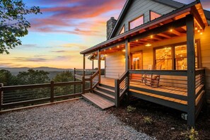 Une maison en bois avec un porche, un escalier et une vue sur les montagnes.