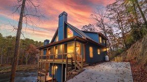 A cabin with a deck overlooking a river, surrounded by trees.