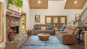 A spacious living room with a stone fireplace, a large sofa set, and a wooden ceiling.