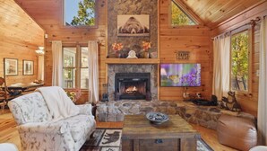 A cozy log cabin interior with a stone fireplace, wooden furniture, and large windows. - Cardinal and Bear Lodge (Blue Ridge)