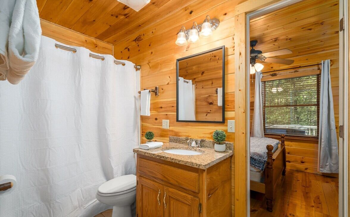 A wooden cabin bathroom with a wooden vanity, a mirror, a sink, and a toilet.