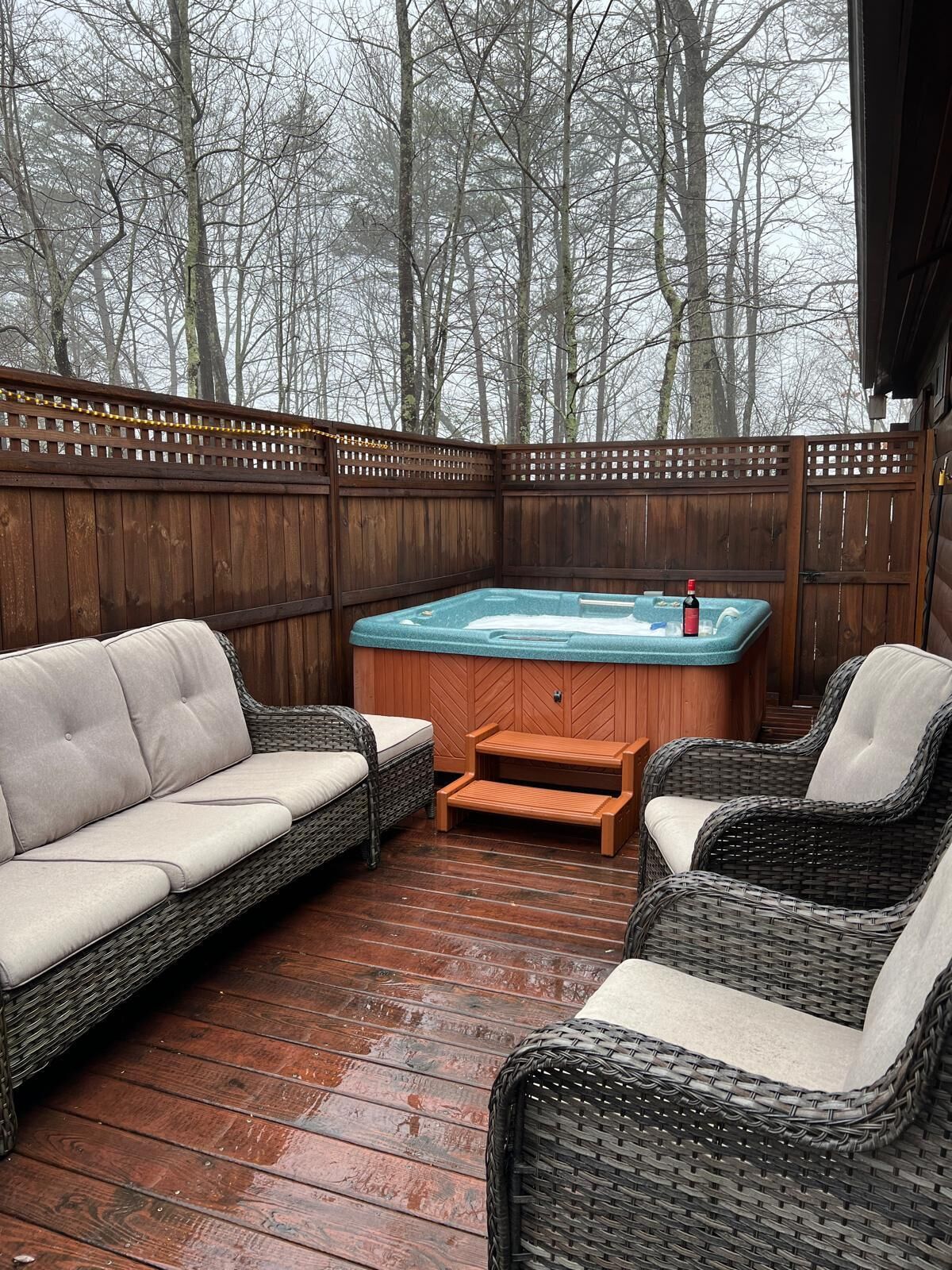 Terraza exterior con jacuzzi, mobiliario de mimbre y valla de madera.