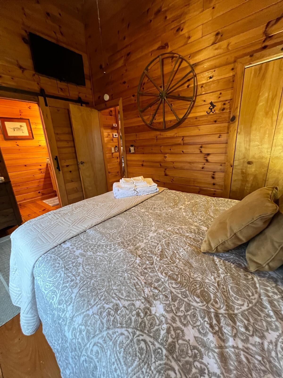 Ein Schlafzimmer in einer Holzhütte mit einem Bett, einem hölzernen Wagenrad und einer Tür zu einem anderen Raum.