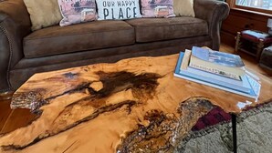 L’intérieur d’un chalet accueillant, avec un mur en bois, un canapé en cuir marron agrémenté de deux coussins et une table basse sur laquelle sont posés des livres.