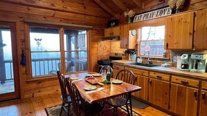 Une cabane en bois comprenant un coin repas, une cuisine et de grandes fenêtres.