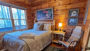 Une chambre confortable dans un chalet en rondins, avec un lit, une chaise, une table de chevet et un tableau accroché au mur.