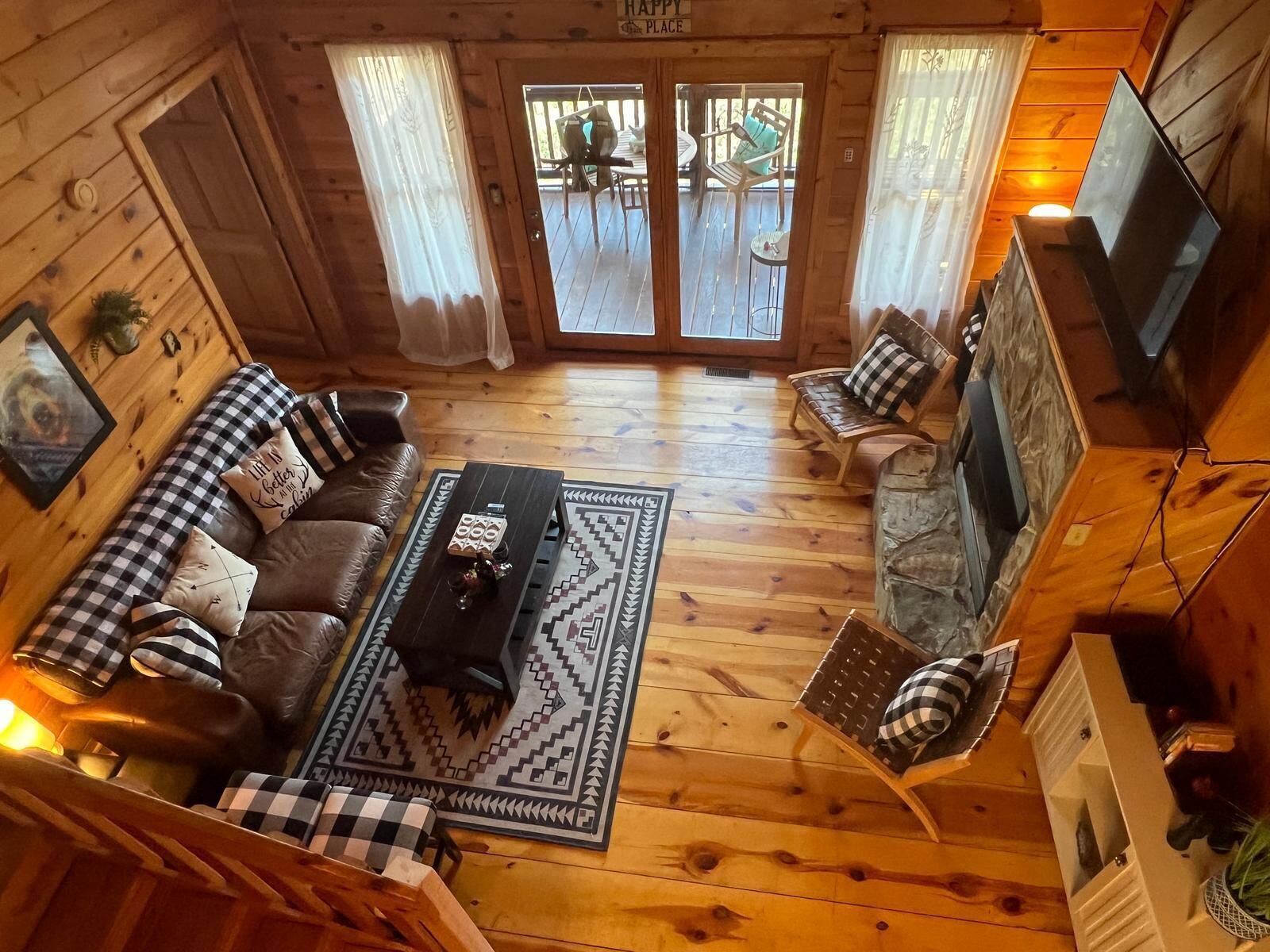A cozy cabin interior with a wooden floor, a sofa set, a coffee table, and a TV mounted on the wall.