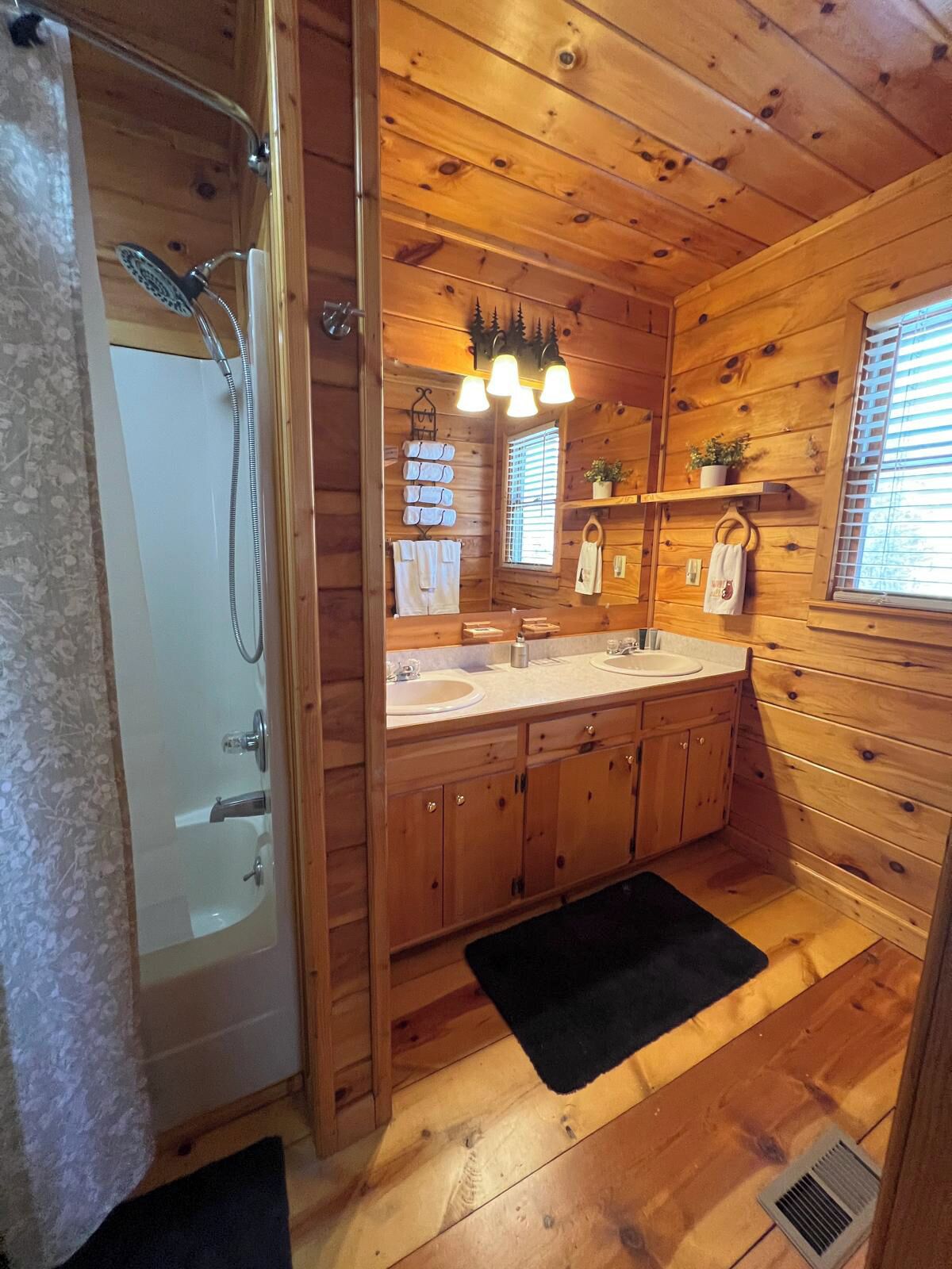 A wooden cabin bathroom with a shower, two sinks, and a vanity.