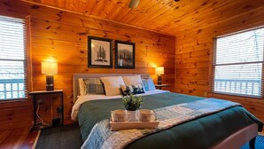Um quarto de cabana de madeira aconchegante, com uma cama grande, duas luminárias de cabeceira e quadros nas paredes.