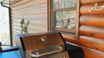 A wooden cabin with a grill and a window with a 'welcome' sign.