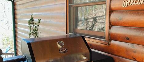 Una cabaña de madera con una parrilla y una ventana con un letrero de 'welcome'.