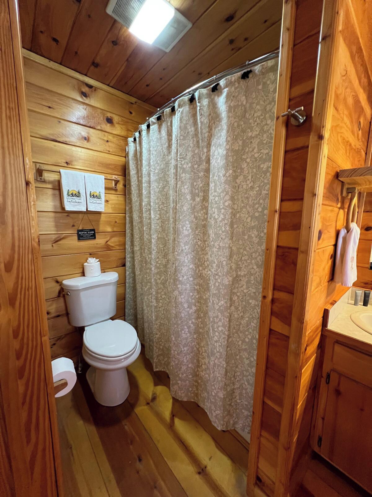 A wooden cabin bathroom with a toilet, shower curtain, and wooden walls.