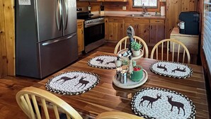 A cozy cabin-style kitchen with wooden walls and ceiling, stainless steel appliances, and a dining table set with placemats featuring animal designs. - Bigfoot's Hideaway | Hot Tub | Fire Pit | Cozy Wooded Retreat (Blue Ridge)