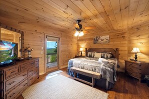 Acogedor dormitorio de cabaña de madera con cama, cómoda, televisor y balcón con vistas panorámicas.